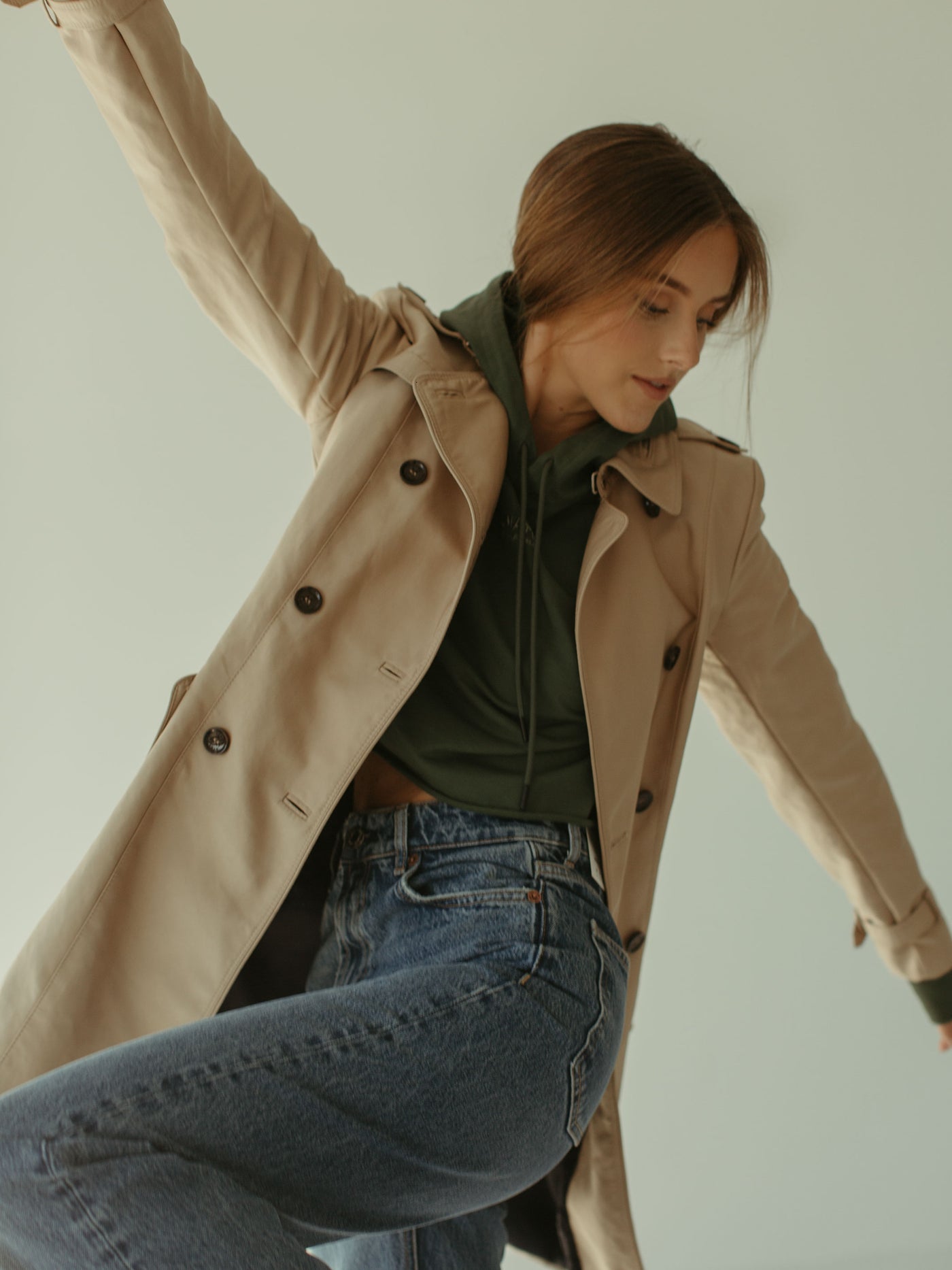 sage cropped hoodie with brand logo and embroidery detail with trenchcoat and relaxed blue jeans